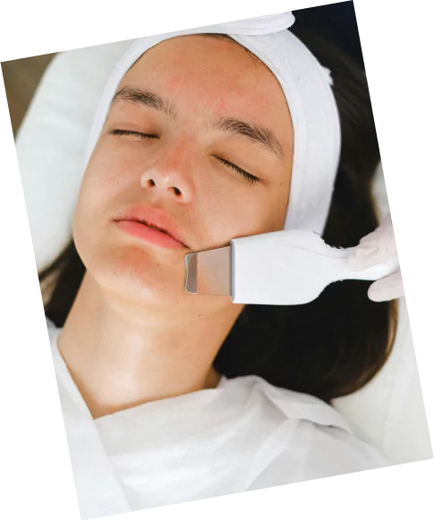 A woman receiving a facial treatment, wearing a white headband, with a serene expression on her face.